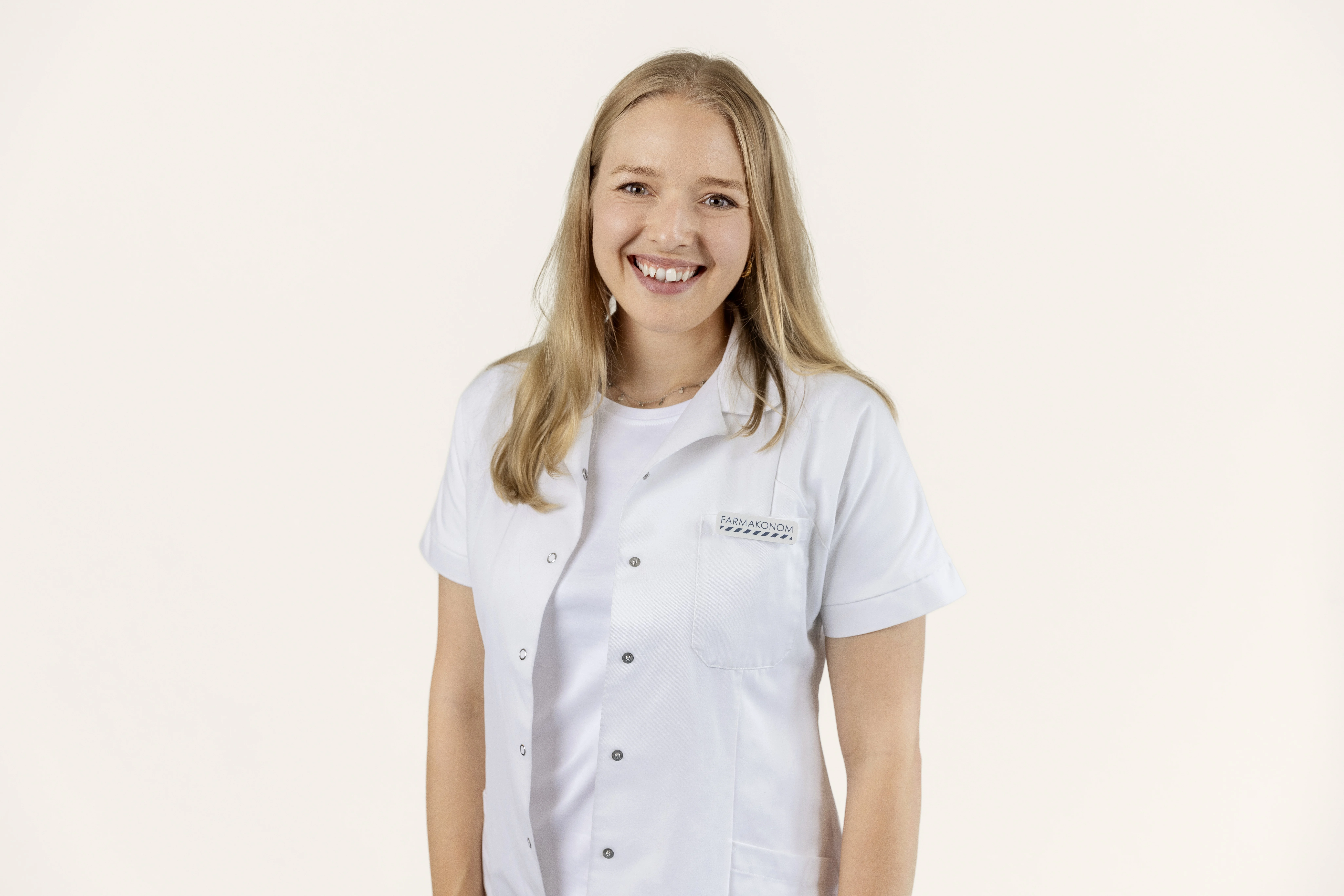 Her ses en smilende farmakonom i hvid kittel på en lys baggrund med teksten “Solpleje til dig med sensitiv hud”