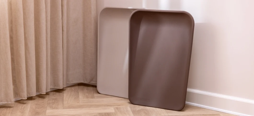 Her ses to Leander opbevaringsbakker i beige og brun placeret på et trægulv ved et gardin.
