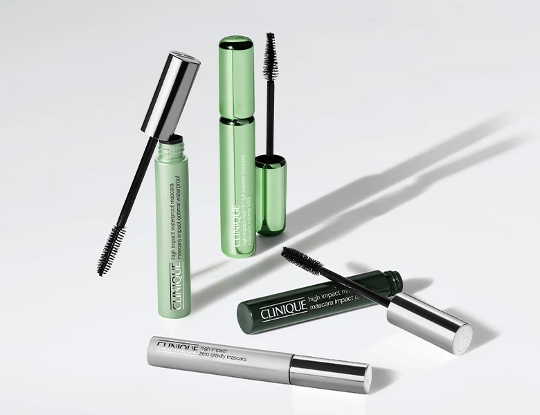 Her ses et billede med mascaraprodukter fra Clinique placeret mod en lys baggrund. Produkterne vises både åbne og lukkede med synlige mascarabørster, og på emballagen står blandt andet “High Impact Mascara” og “High Impact Zero Gravity Mascara”.