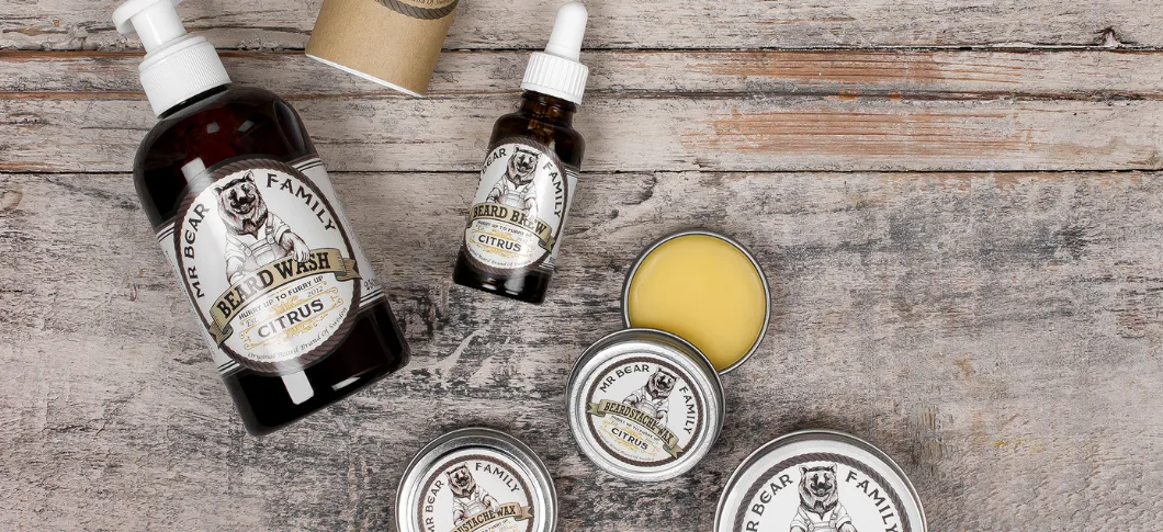 Mr. Bear Family citrus-produkter til skægpleje ligger spredt på et rustikt træbord, herunder beard wash, beard brew og beard balm i brun emballage.