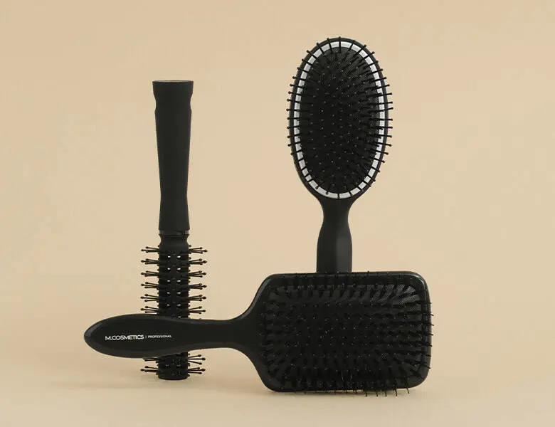 Her ses tre sorte M.Cosmetics hårbørster på en beige baggrund.