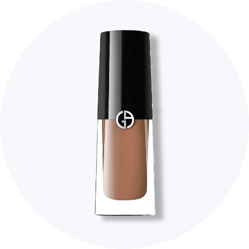 Her ses et billede af et makeup-produkt fra Giorgio Armani placeret centralt mod en lys, rund baggrund. Produktet er i klart glas med sort låg og har Giorgio Armani-logo på fronten.