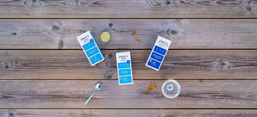 Her ses tre forskellige Eskio-3 produkter, som ligger på en træterrasse, hvor der, bl.a., ved siden af ligger en ske og et glas vand.