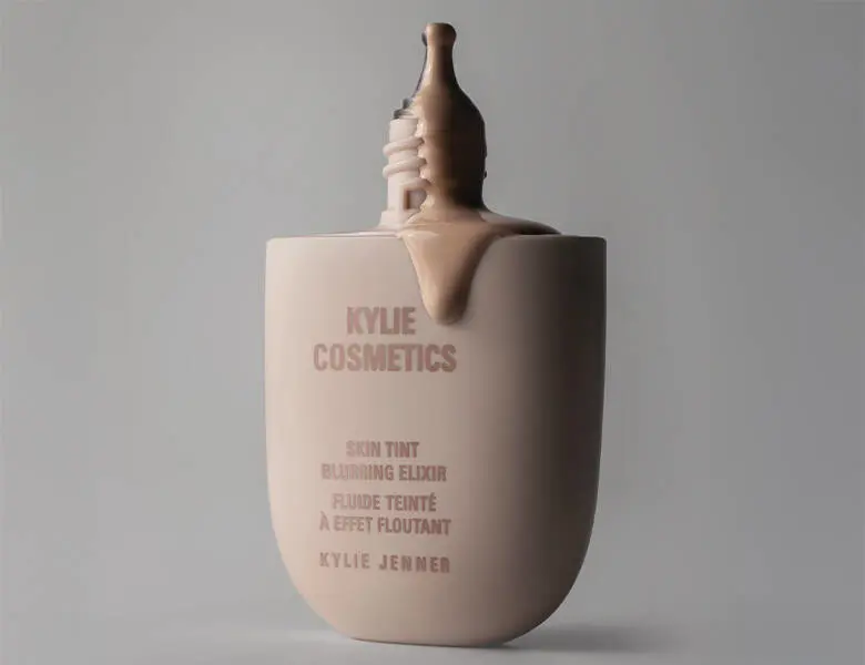 Her ses en grå baggrund med et Kylie Cosmetics produkt i midten. Produktet er åbent og noget af skin tinten kommer ud.