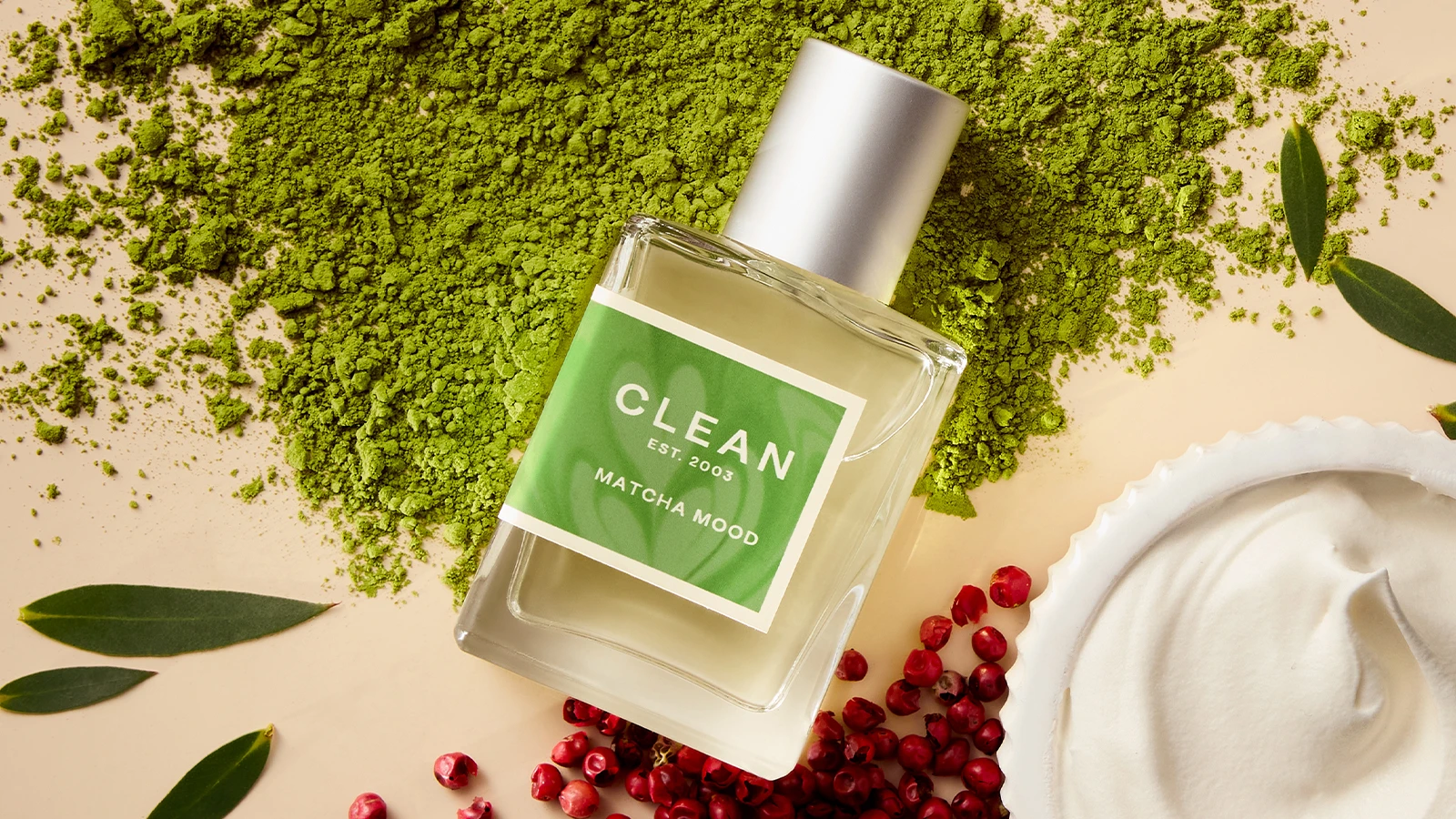 Her ses CLEAN Matcha Mood i en transparent parfumeflakon med grøn etiket og sølvfarvet låg. Flakonen ligger blandt grønt matchapulver, grønne blade og røde bær.