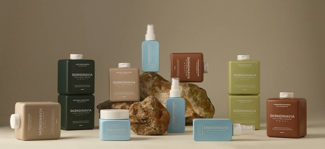 Her ses et billede med flere hårplejeprodukter fra Skøndinavia placeret omkring sten mod en beige baggrund. På produkterne står bl.a. teksten “SKØNDINAVIA MULTIVITAMIN HAIRCARE”. Produkterne er i forskellige farver som grøn, blå, beige og brun.