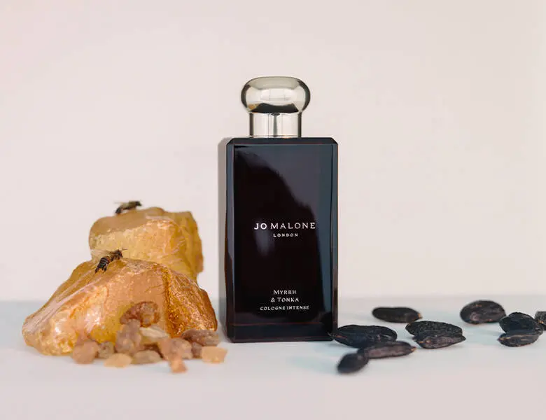 Her ses en beige baggrund med en sort Jo Malone London cologne. I siderne er der sten og rav.