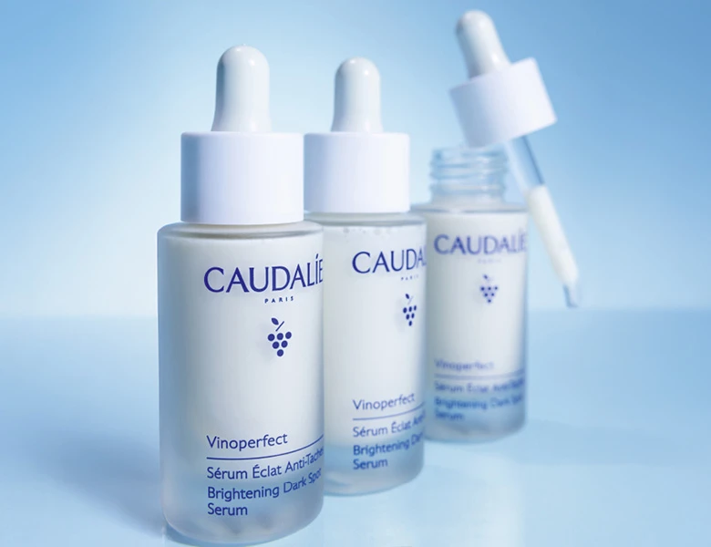 Her ses CAUDALIE serummer i glasflasker med pipette på en blå baggrund.