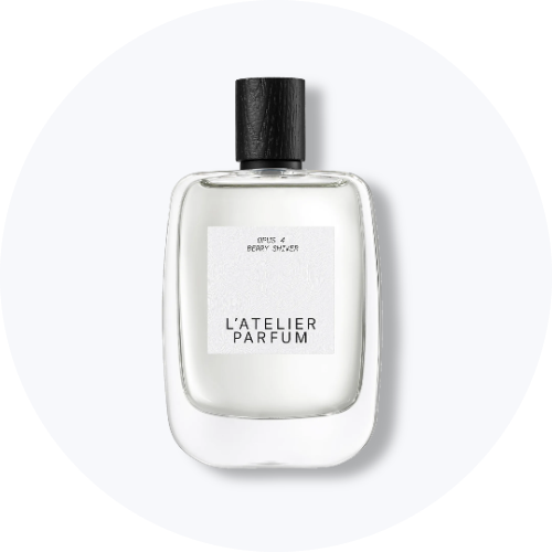 Her ses et billede af en parfumeflakon fra L’Atelier Parfum placeret centralt mod en lys, rund baggrund. På flakonen står teksten “L’ATELIER PARFUM”. Flakonen er i klart glas med sort låg og hvid label.