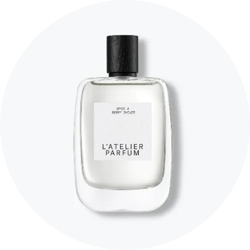 Her ses et billede af en parfumeflakon fra L’Atelier Parfum placeret centralt mod en lys, rund baggrund. På flakonen står teksten “L’ATELIER PARFUM”. Flakonen er i klart glas med sort låg og hvid label.