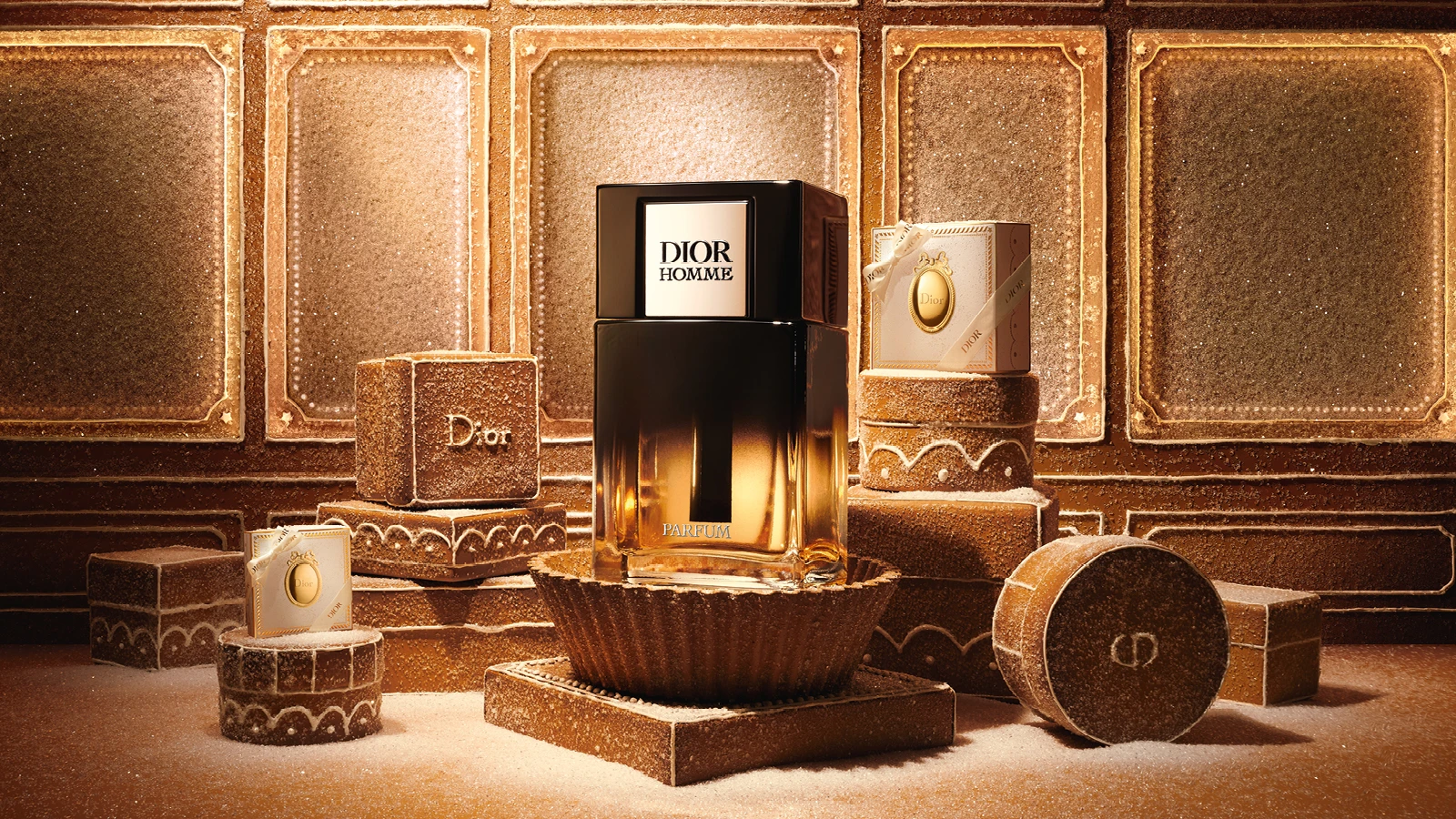 Dior Homme Parfum flaske i sort og guld, omgivet af sukkerdækkede honningkagedekorationer, der inkluderer logoer for 'Dior' og 'CD'.