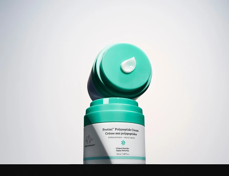 Her ses en Drunk Elephant ansigtscreme i hvid og turkis emballage med creme på låget.