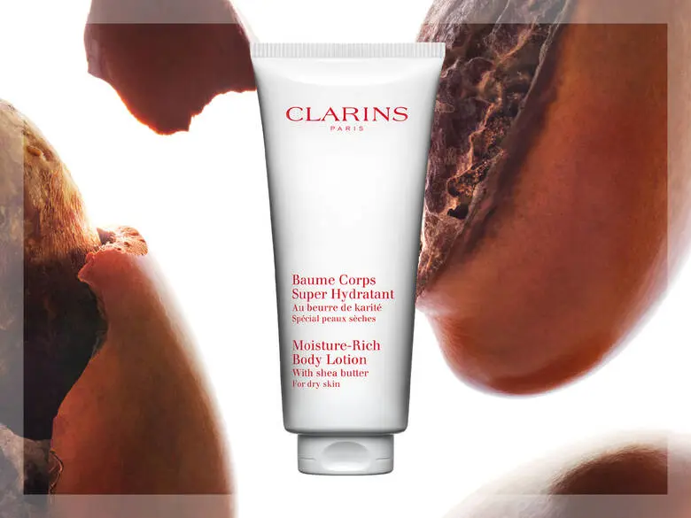 Her ses en hvid baggrund med nogle brune nødder og et hvid Clarins produkt i midten.