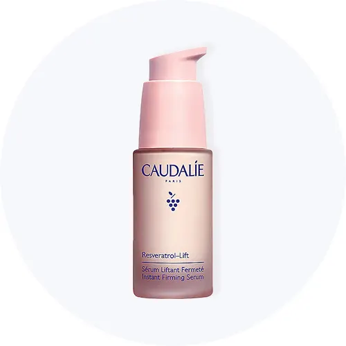Her ses Caudalie Resveratrol-Lift Instant Firming Serum i en lyserød flaske på en lysegrå cirkel.