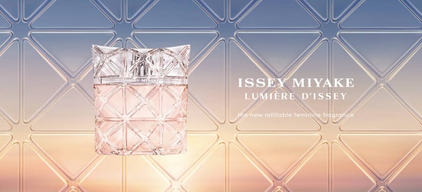 Her ses en issey miyake parfume i en firkantet, pudderfarvet flakon. Baggrunden ligner en solnedgang med blå og orange nuancer. Til føjre for parufmen står der "Issey Miyake Lumière d'issey The new refillable feminine fragrance".