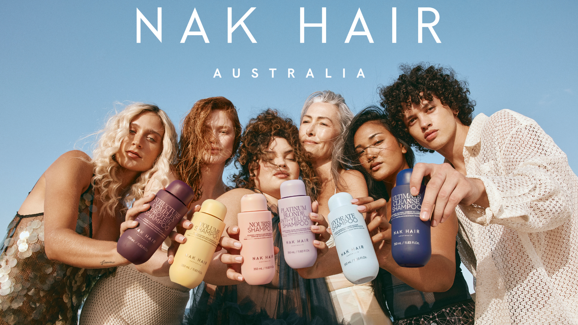 Her ses et billede af seks personer med forskellige hårtyper og hårfarver samlet mod en blå himmel. De holder hver især hårplejeprodukter fra NAK Hair, og øverst står teksten “NAK HAIR AUSTRALIA”. Produkterne omfatter blandt andet shampoo til forskellige hårtyper i farverige flasker.