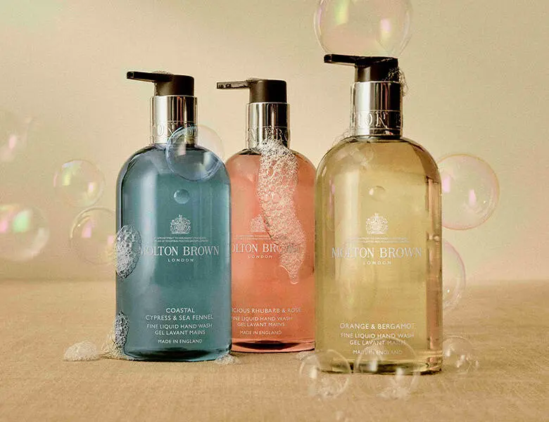 Her ses tre produkter fra Molton Brown i forskellige farver. Baggrunden er lys og har sæbebobler og sæbeskum. 