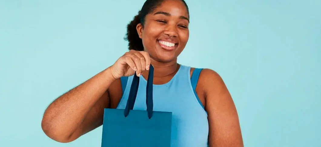 Her ses en smilende person der holer en gavepose foran en blå baggrund.