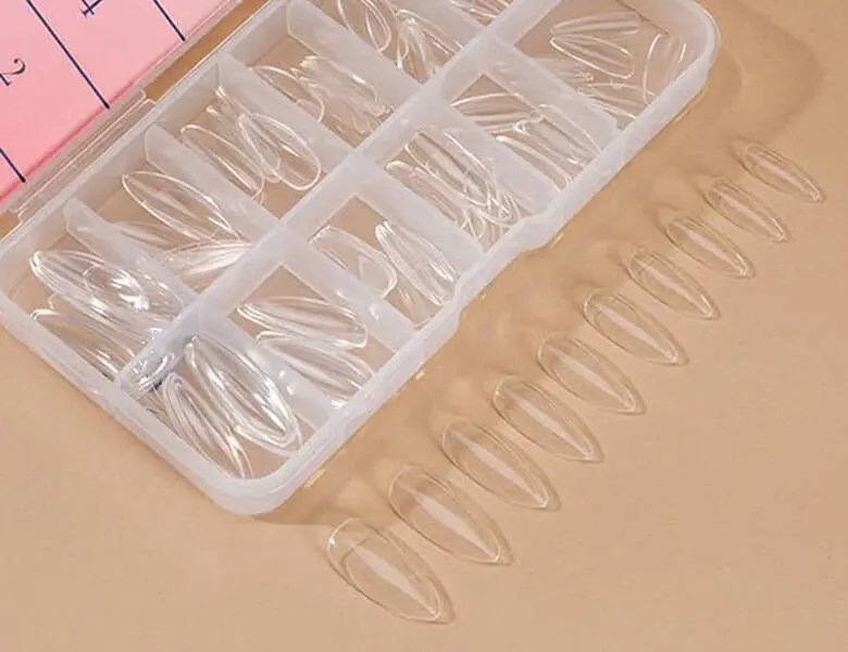 Her ses nogle falske negle fra Nailster på beige baggrund.