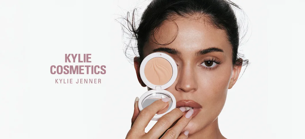 Her ses en Kylie Jenner, der holder en Kylie Cosmetics pudder foran ansigtet med teksten "Kylie Cosmetics by Kylie Jenner".