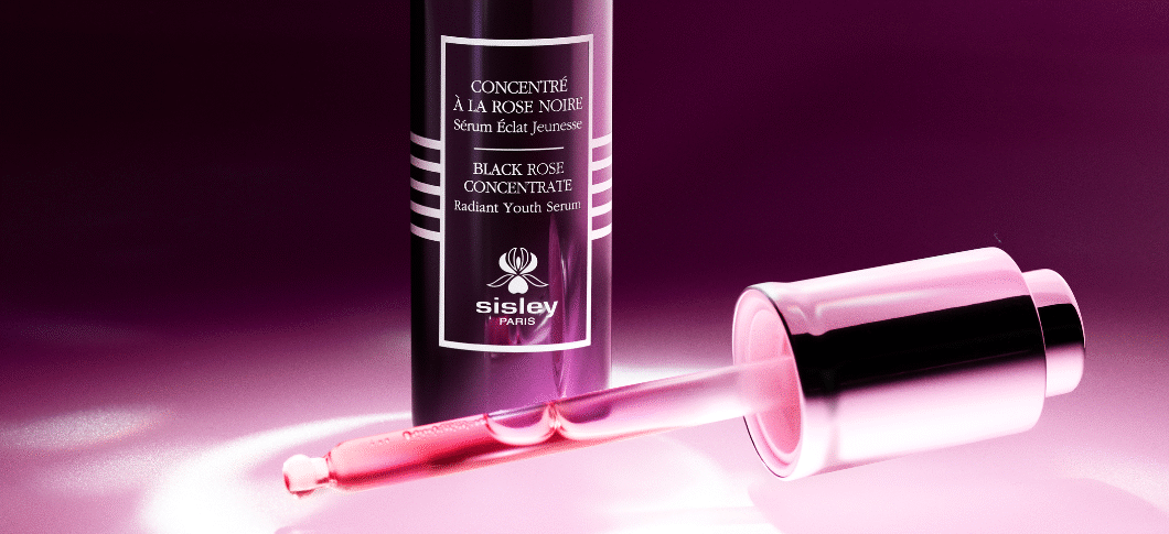 Her ses et Sisley Black Rose Cencentrate serum på en mørkelilla baggrund. Pipitten fra flasken ligger foran produktet.