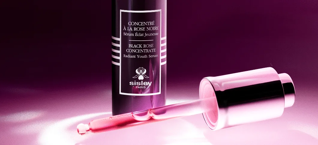 Her ses et Sisley Black Rose Cencentrate serum på en mørkelilla baggrund. Pipitten fra flasken ligger foran produktet.