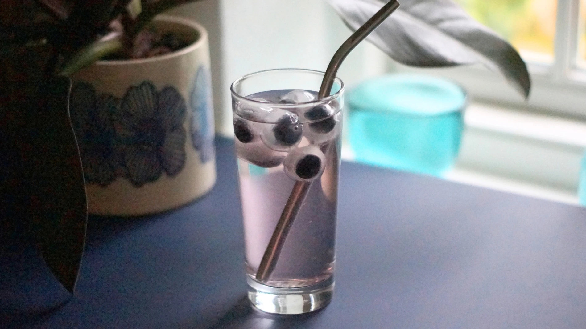 Glas med lilla drink, isterninger, flydende øjeæble-dekorationer og et metalsugerør.