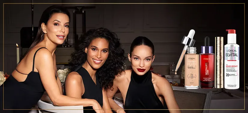 Her ses tre kvinder beklædt i sort. Til højre for dem ses flere forskellige L'Oréal Paris produkter. Baggrunden er mørk.