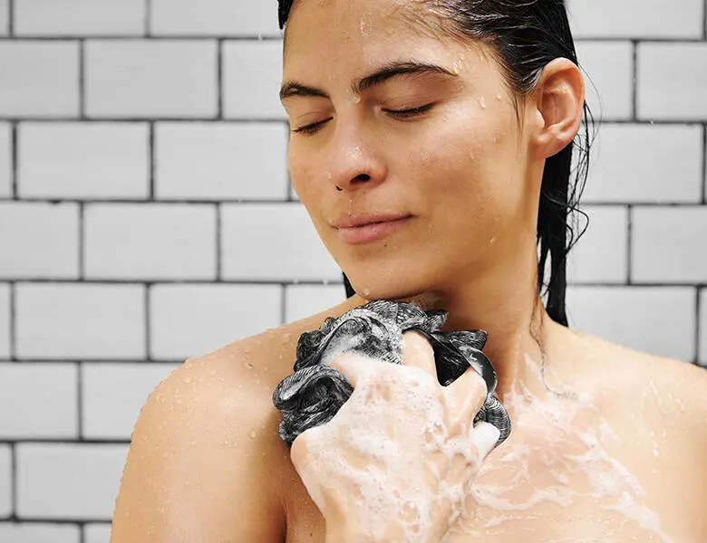 Her ses en kvinde i badet. Hun holder en loofah med sæbe op foran sig.
