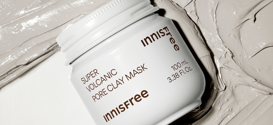 Her ses en Innisfree clay mask i en hvid krukke på en lys baggrund med ler.