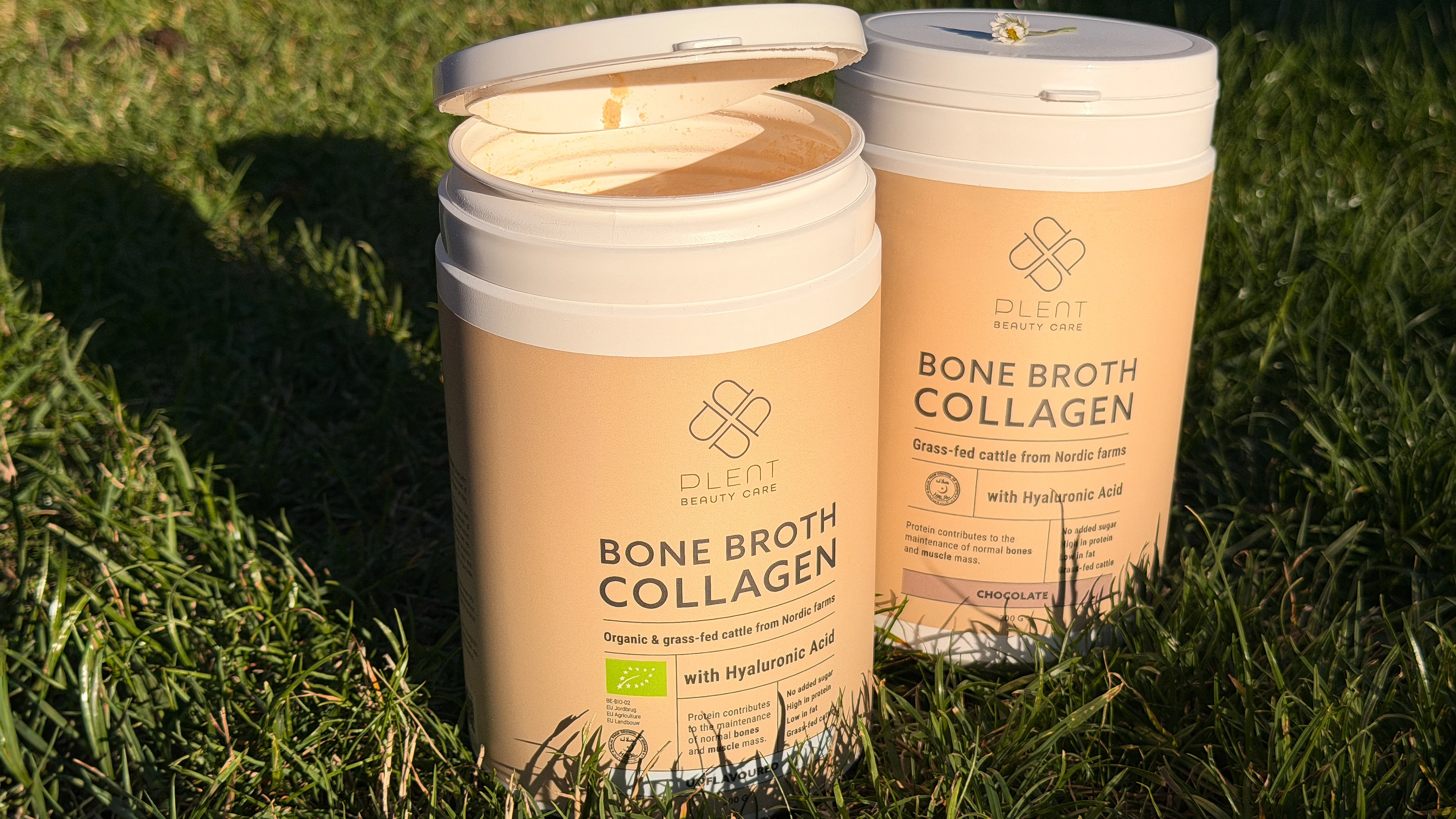 To Plent Beauty Care Bone Broth Collagen beholdere står på græs. Den ene er åben og viser pulveret. Mærket 'Organic & grass-fed cattle from Nordic farms' og 'with Hyaluronic Acid'.