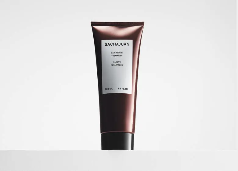 Her ses et billede af et hårprodukt fra SACHAJUAN placeret centralt mod en lys baggrund. På produktet står teksten “SACHAJUAN Hair Repair Treatment”. Produktet er i en mørk, metallisk tube med sort låg.