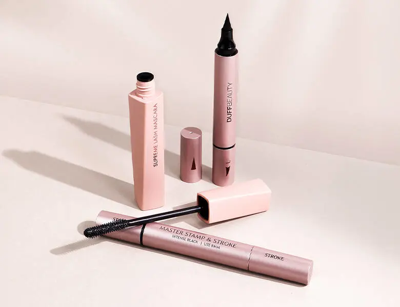 Her ses nogle forskellige makeupprodukter fra DUFFBEAUTY på en lys lyserød baggrund.