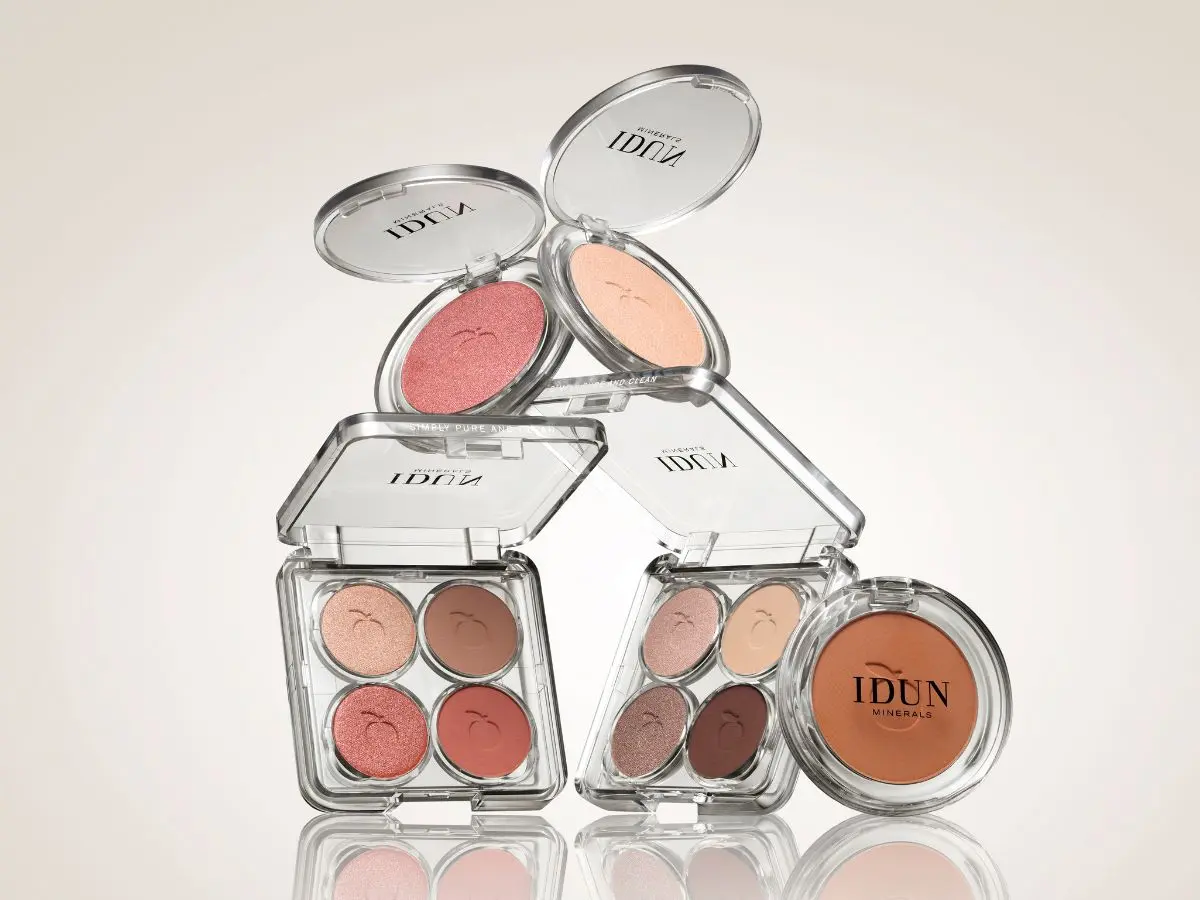 Her ses et billede med øjenmakeup fra IDUN Minerals mod en lys baggrund. Produkterne omfatter to åbne øjenskyggepaletter med fire nuancer hver, to åbne single eyeshadows og en bronzer eller pudder. De gennemsigtige etuier gør farverne synlige og fremhæver de varme, naturlige nuancer.