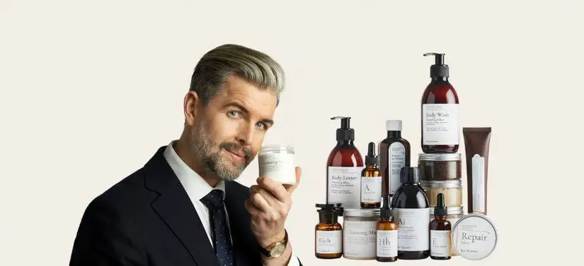Her ses en mand i jakkesæt til venstre for en masse Raz Skincare produkter. Manden holder desuden også ét produkt. Baggrunden har en meget lysegul farve.