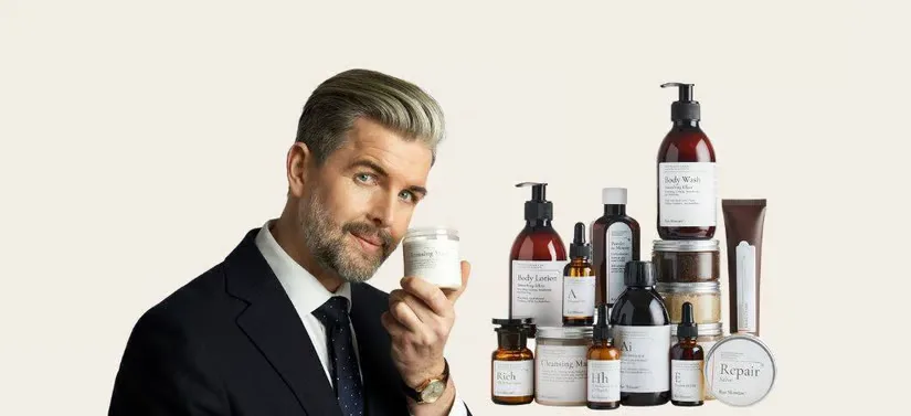 Her ses en mand i jakkesæt til venstre for en masse Raz Skincare produkter. Manden holder desuden også ét produkt. Baggrunden har en meget lysegul farve.