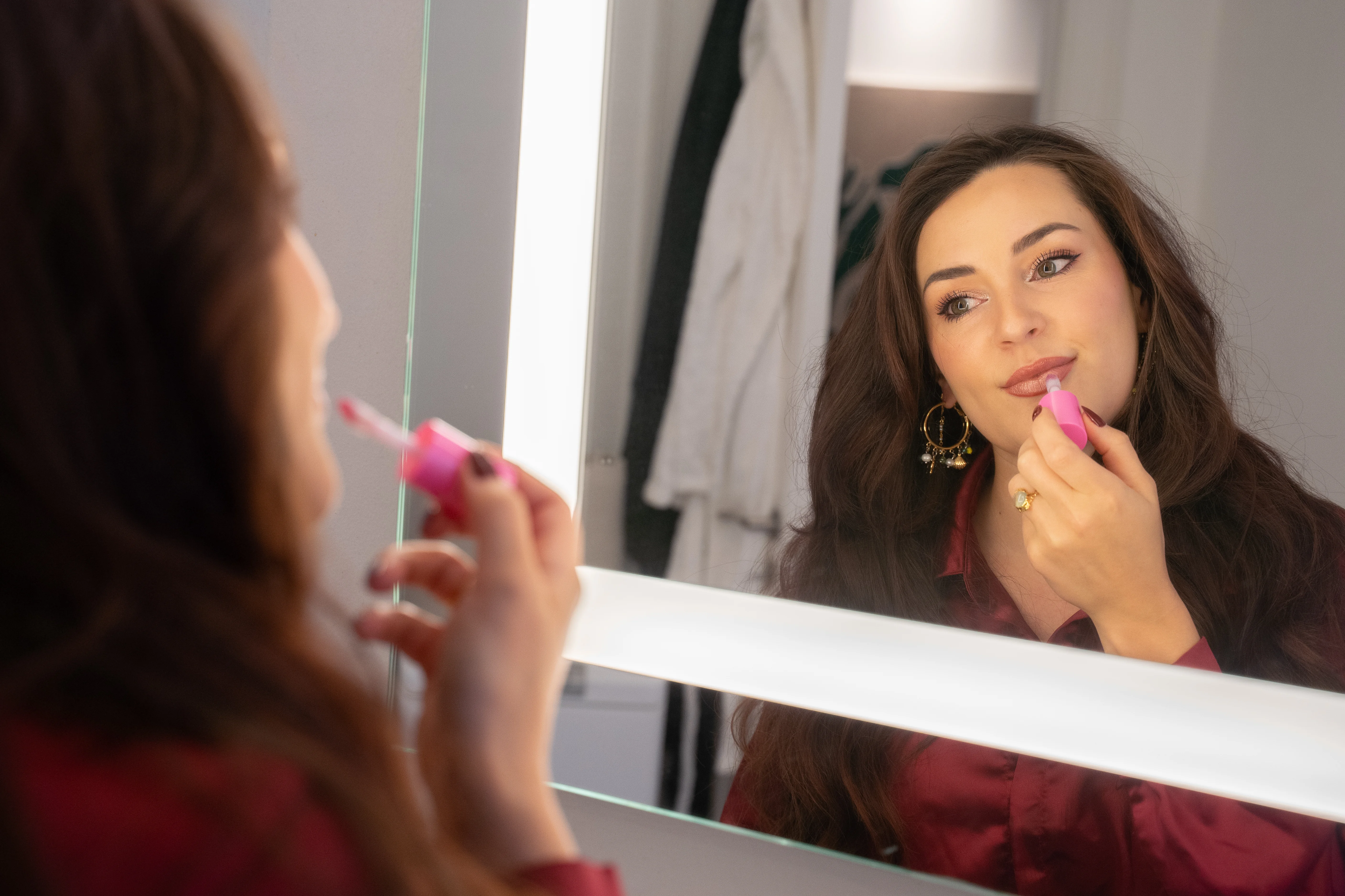 Kvinde, der påfører lipgloss i spejl 