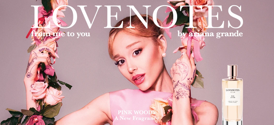 Her ses en person omgivet af lyserøde blomster og bånd med parfumeflasken Lovenotes Pink Woods. Baggrunden er lyserød. Teksten på billedet er: "LOVENOTES", "from me to you", "by ariana grande" og "PINK WOODS – A New Fragrance".