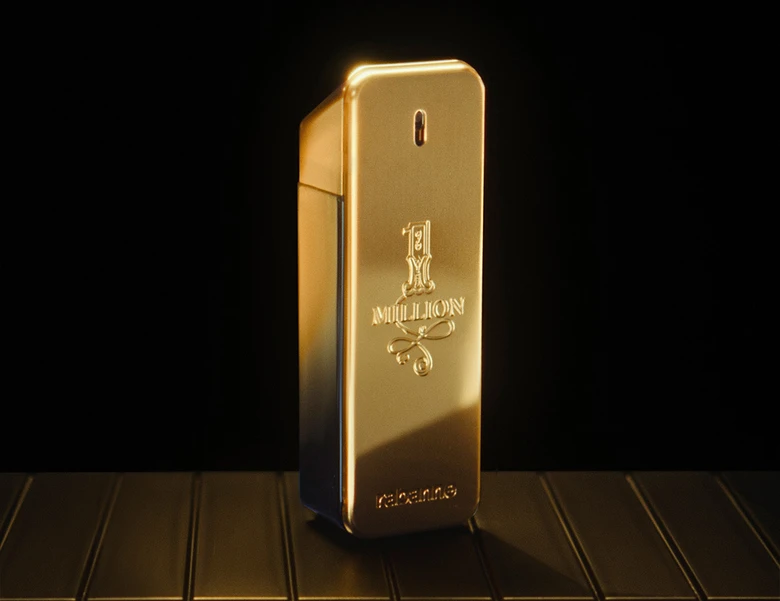 Her ses et billede af en parfumeflakon med teksten “1 MILLION” placeret mod en mørk baggrund. Flakonen er i guldfarvet, rektangulært design med blank overflade.