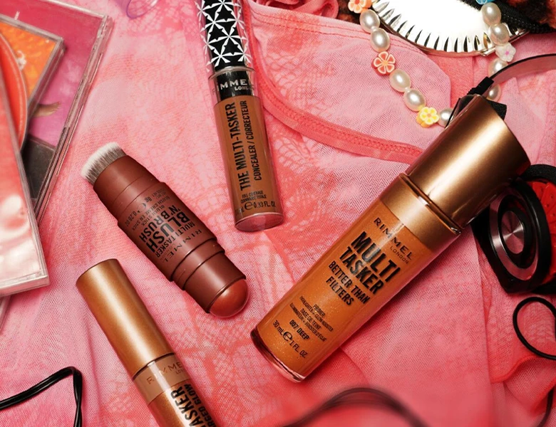 Her ses et billede med forskellige ansigtsprodukter fra Rimmel London placeret på en pink baggrund med accessories omkring. På produkterne står blandt andet “MULTI TASKER” og “BLUSH”.