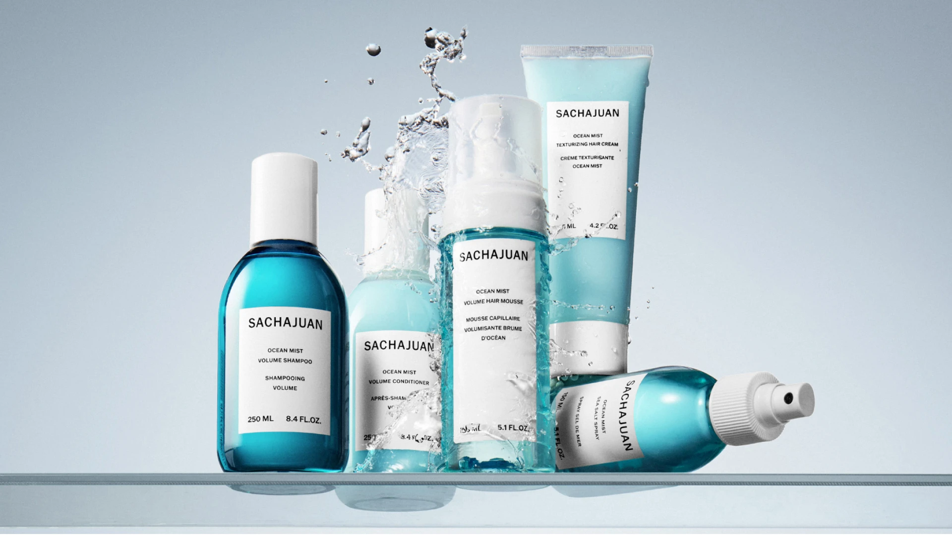 En samling af SACHAJUAN Ocean Mist hårprodukter inklusive shampoo, balsam, mousse og spray, med vandstænk.