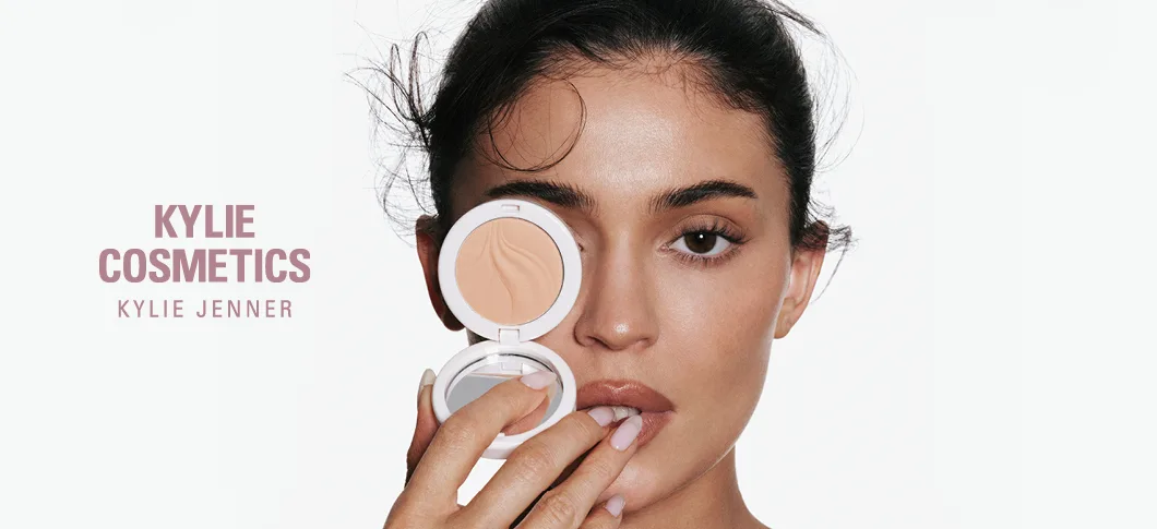 Her ses en person, der holder en Kylie Cosmetics pudder foran ansigtet med teksten "Kylie Cosmetics by Kylie Jenner".