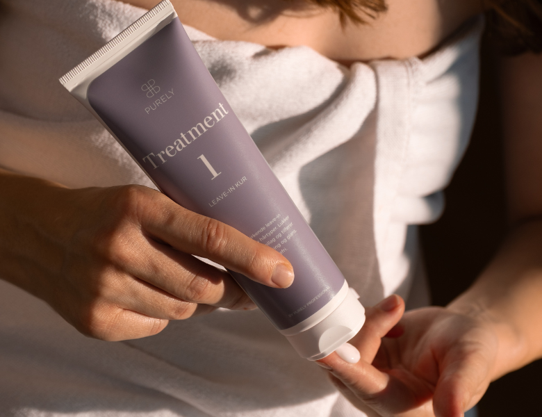 Her ses et billede af en person, der holder et hårplejeprodukt fra Purely Professional i hånden. På tuben står teksten “Treatment 1”, og produktet påføres i hånden.