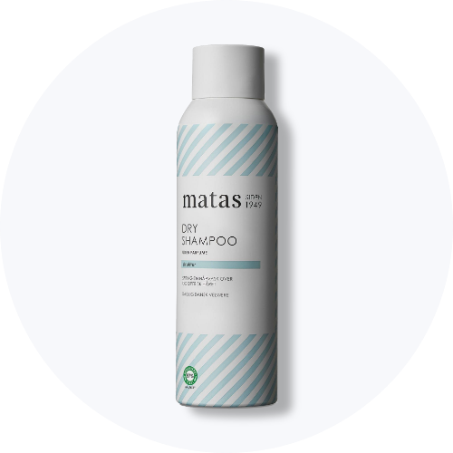 Her ses et billede af en dry shampoo fra Matas placeret centralt mod en lys, rund baggrund. På flasken står teksten “matas DRY SHAMPOO”. Flasken er i hvid med lyseblå stribede detaljer.