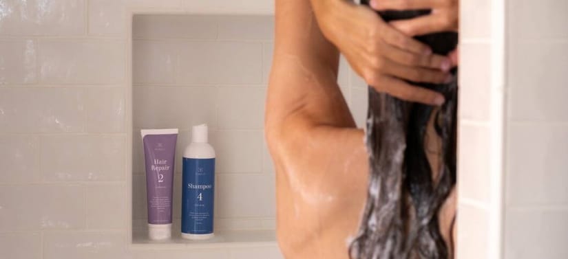 Her ses et billede med en person i bad, hvor håret vaskes med shampoo. I baggrunden står to produkter på en hylde med teksten “Hair Repair” og “Shampoo 4”.