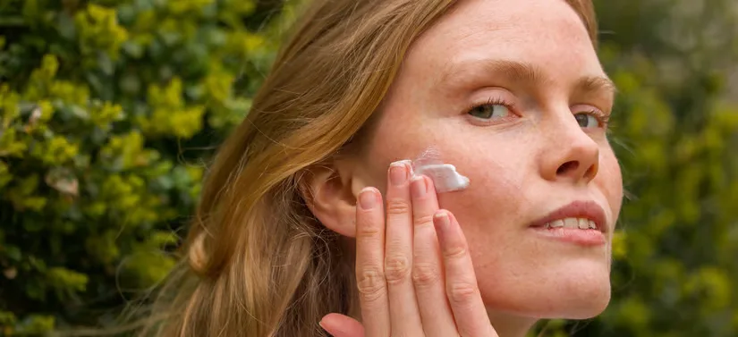 Her ses en kvinde, som er udenfor. Hun er ved at smøre creme i ansigtet. 