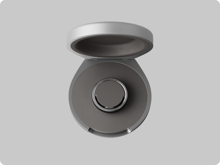 En grå, åben rund kompakt enhed med et cirkulært element i midten. Transpotable oplader til Oura Ring 5