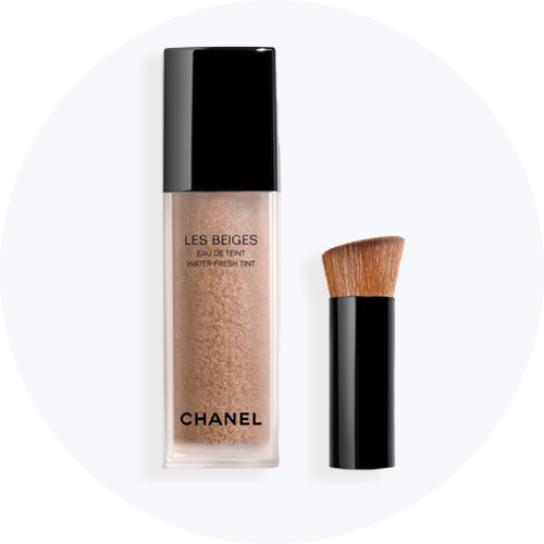 Her ses Chanel Les Beiges Eau de Teint Water-Fresh Tint i en transparent flaske med sort låg sammen med en tilhørende makeupbørste.