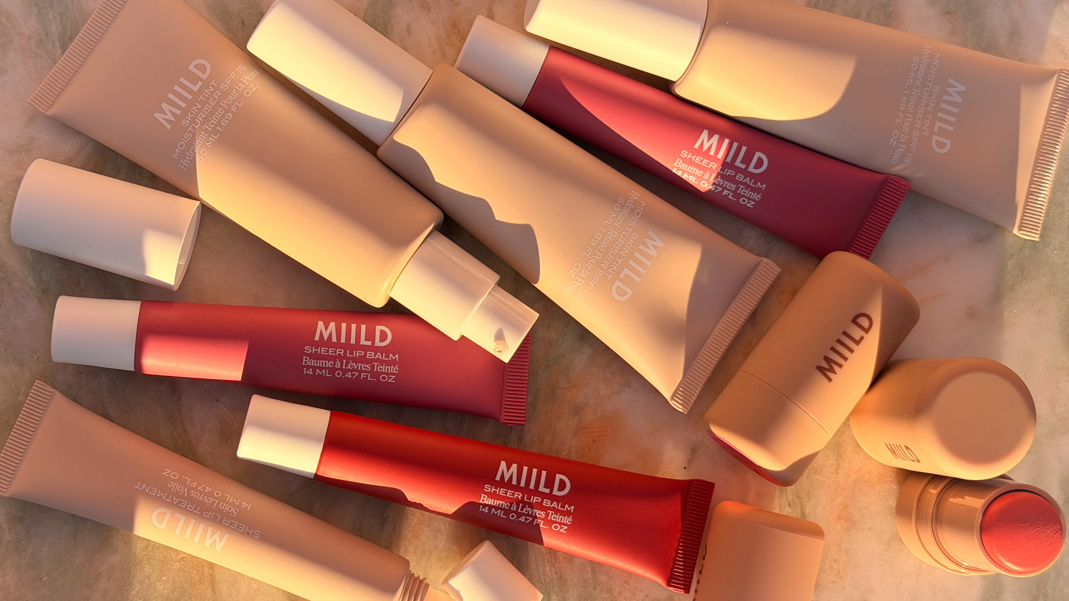 Et udvalg af MIILD kosmetik: beige tuber med Skin Tint, røde tuber med Lip Balm, og en beige makeup-stick.