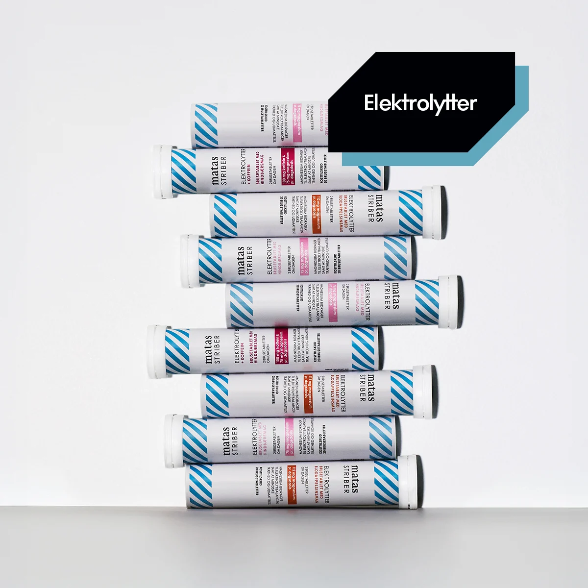Her ses et udvalg af Matas Striber Elektrolytter brusetabletter stablet på en hvid baggrund med lyseblå diagonale striber langs kanten. Teksten "Elektrolytter" står nederst på billedet.